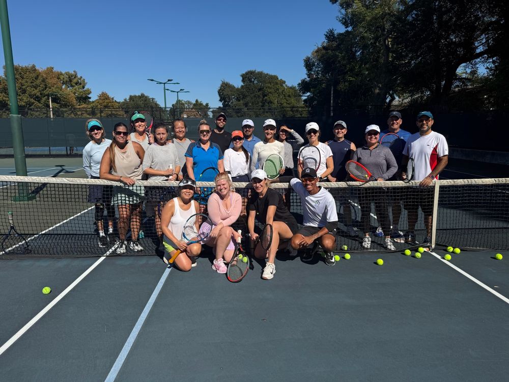 A full clinic group posing at the net with balls scattered on court